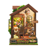 A miniature butterfly-themed cottage with a brown wooden roof, beige exterior walls, and a detailed interior decorated with butterflies, plants, a rocking chair, and small accessories, shown on a plain white background.