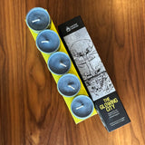 Set of blue candles in a yellow holder with a branded box on a wooden surface