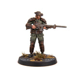 A painted tabletop miniature figurine of a cowboy soldier holding a large machine gun, standing on a round textured base with small grass tufts, photographed against a plain white background.