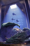 Dragon-like creature with people on ropes inside a large tank, possibly a museum exhibit.