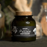 A dark green glass jar candle with a cork stopper and a black label reading 'Poison Garden Sample No. 14: Henlock Conium Maculatum', photographed in a moody, softly blurred setting.