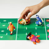 Colorful toy figures on a green playing field with a hand interacting with one of them.