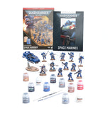 Warhammer 40k Space Marines miniatures kit on a white background, including painted blue space marine figures, a blue vehicle, multiple paint bottles, a brush, and two product boxes.