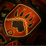 A close-up of a decorative shield-shaped object featuring a red and black design with a gold paw print, chain motif, and circular emblem.