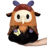 Plush toy resembling a creature with brown fur, purple horns, and black eyes held in a hand against a white background.