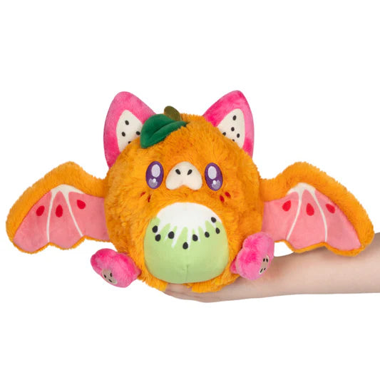 Plush toy resembling a fruit with bat wings held by a hand on a white background
