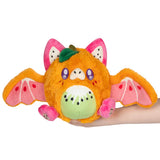 Plush toy resembling a fruit with bat wings held by a hand on a white background