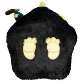 Black plush toy with yellow feet and a small green object on a white background