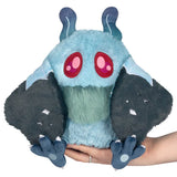Plush toy with blue body, pink eyes, and black wings held by a hand on a white background