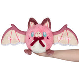 Pink plush toy with bat wings held by a hand on a white background