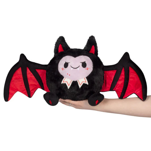 Plush toy bat with red wings held by a hand on a white background