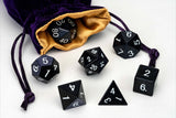 Set of black polyhedral dice with a purple drawstring bag on a white background