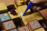Close-up of a hand using a blue tool to interact with a small figurine on a colorful tile-based game board.
