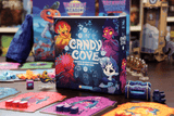 Board game box titled 'Candy Cove' with game pieces and cards on a table.