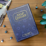 Blue book titled 'The Map Library' on a wooden surface with dice and gaming accessories.