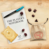 The Player's Notebook with dice and accessories on a wooden surface