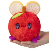 Plush toy resembling a red fruit with mouse ears held in a hand on a white background
