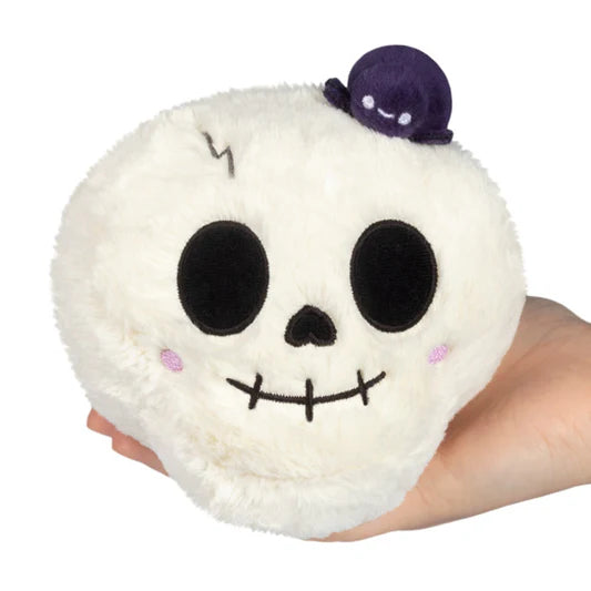 Plush toy shaped like a skull with a hand holding it on a white background