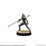 A painted fantasy miniature figurine of a hooded warrior holding a long red staff, posed on a round black base with faux grass and gravel. The figure is mostly black with small red, yellow, and white details.