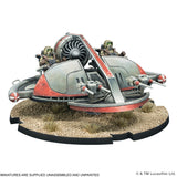 A painted miniature sci-fi vehicle or station model displayed on a textured desert-style base, photographed against a plain white background. The model has a metallic gray and red body with small green-tinted figures and mechanical details visible.