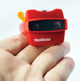 A red ViewMaster handheld video camera being held in a person's hand against a plain white background.