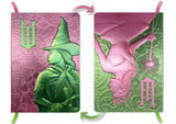 Two decorative books with embossed designs of a witch and a fairy on pink and green covers.